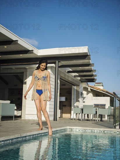 Hispanic woman dipping toe in swimming pool