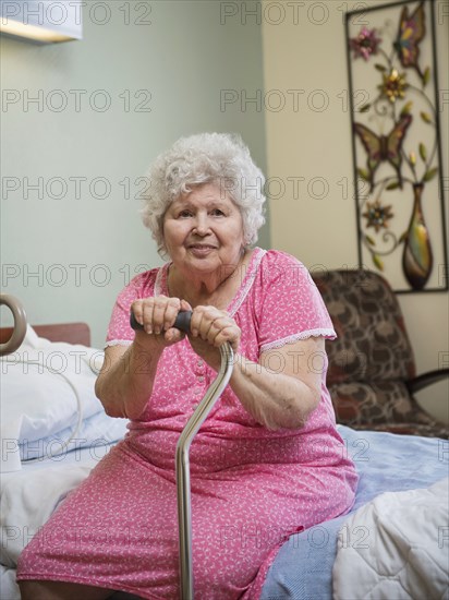 Smiling Caucasian woman sitting on bed leaning on cane