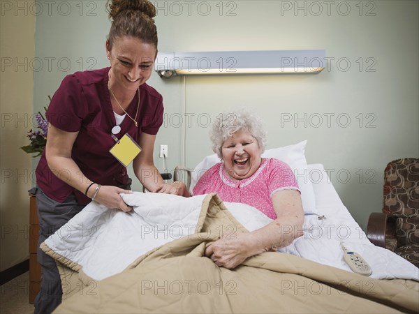 Caucasian nurse with laughing patient in hospital bed