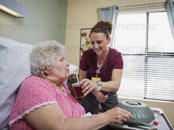 Caucasian nurse feeding patient in hospital bed