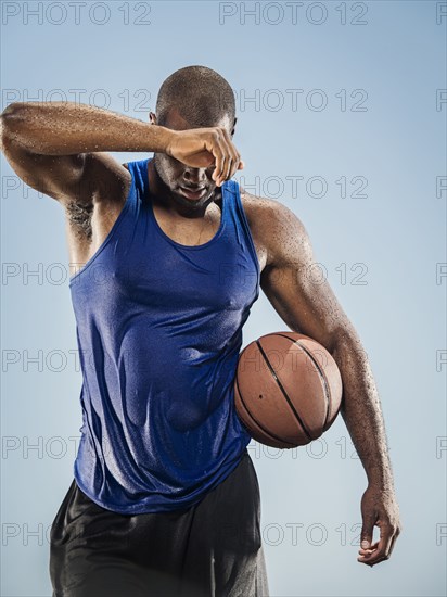 Black man holding basketball wiping sweat off forehead