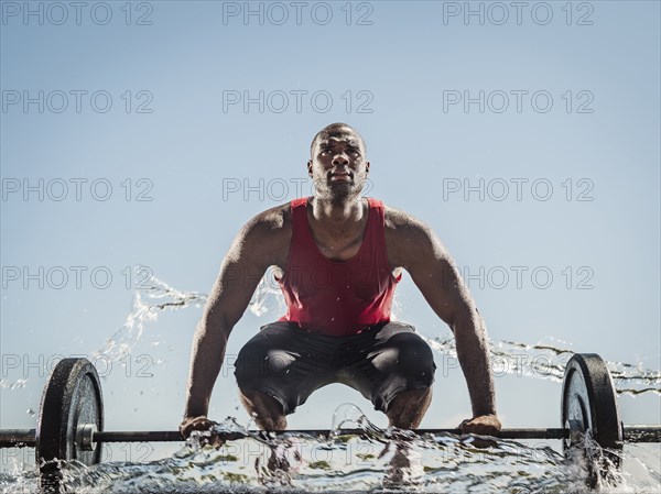Water spraying on black man preparing for lifting barbell