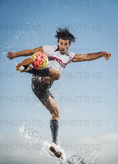 Water spraying on Hispanic man kicking soccer ball