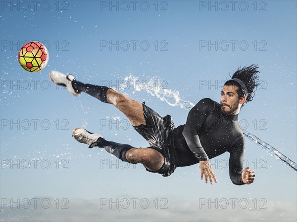 Water spraying on Hispanic man kicking soccer ball