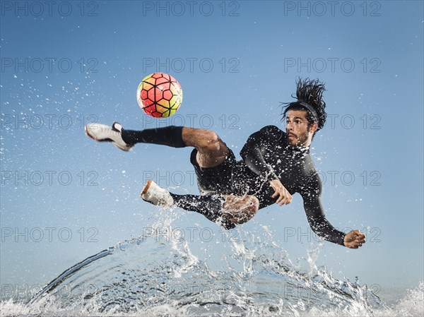 Water spraying on Hispanic man kicking soccer ball