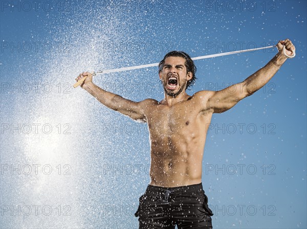 Water spraying on Hispanic man holding jump rope