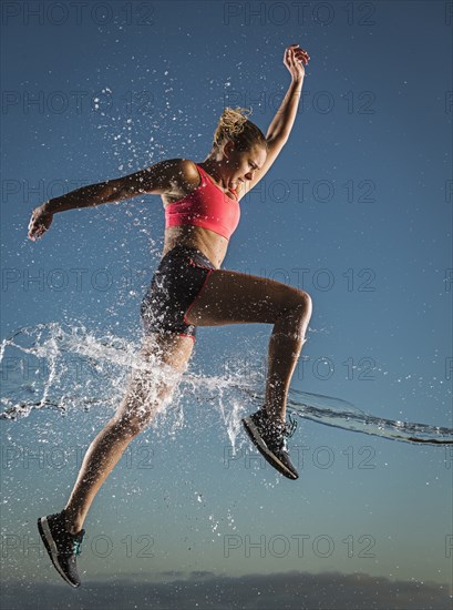 Water splashing on Caucasian woman running in sky