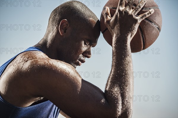 Portrait of sweating Black man touching forehead with basketball