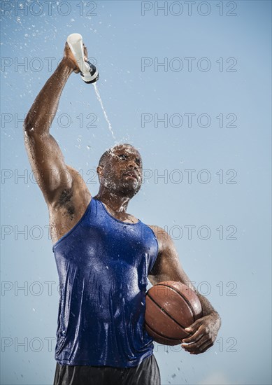 Black man holding basketball cooling off with water bottle