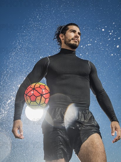 Water splashing on Hispanic man holding soccer ball