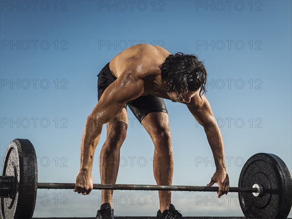 Sweating Hispanic man lifting barbell