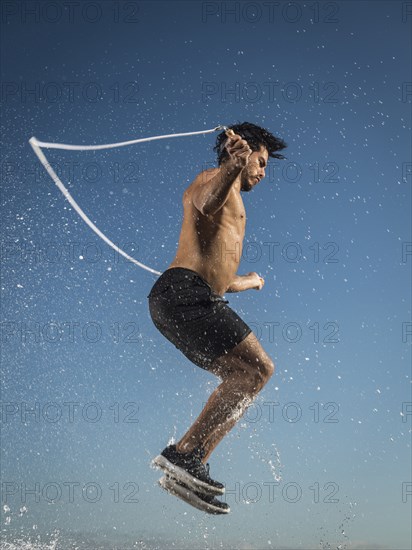 Water splashing on Hispanic man jumping rope