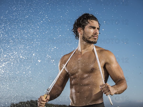 Water splashing on Hispanic man holding jump rope