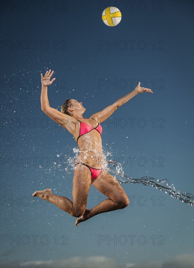 Water splashing on Caucasian woman jumping to volleyball