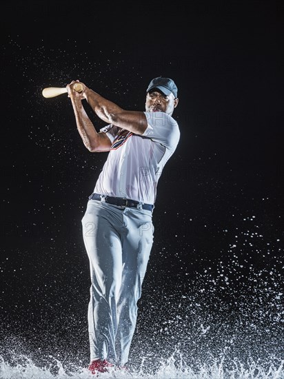 Water splashing on Black baseball player swinging bat