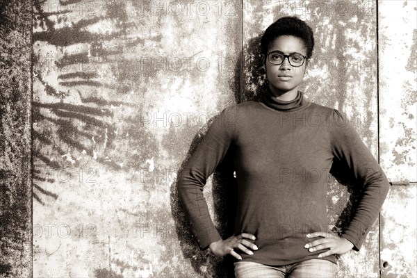 Serious African American woman leaning on rusty metal wall