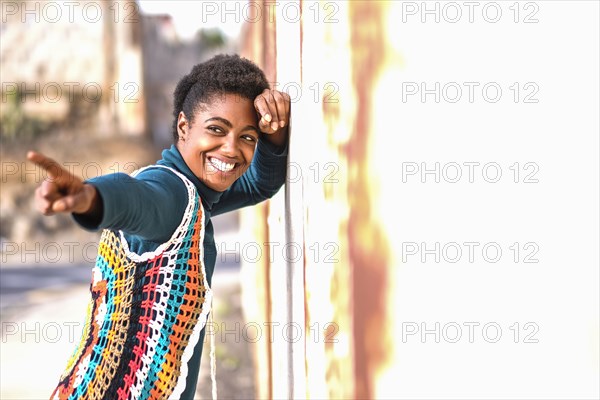Smiling African American woman leaning on wall and pointing finger