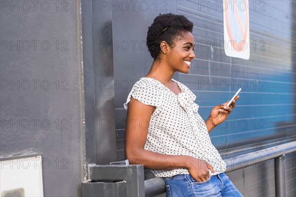 African American woman leaning on railing texting on cell phone