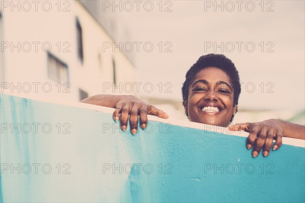 Smiling African American woman peering over blue wall