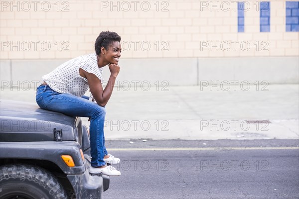 Smiling African American woman sitting on hood of car