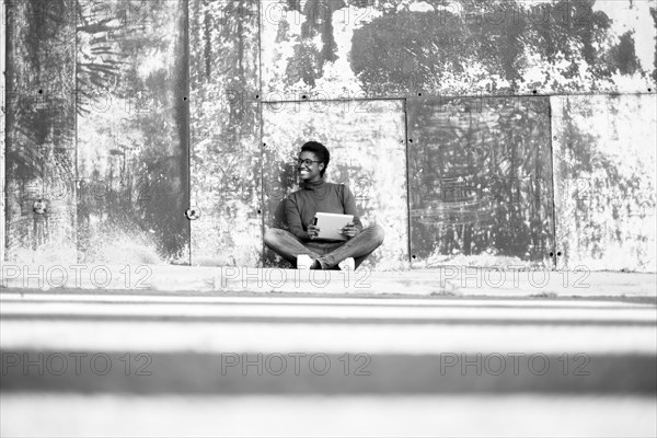 Distant African American woman sitting on ground using digital tablet
