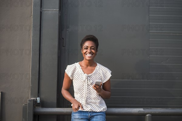 Smiling African American woman leaning on railing texting on cell phone