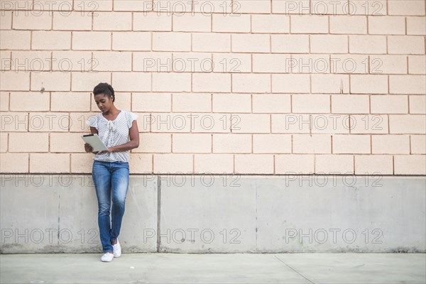 African American woman leaning on concrete wall using digital tablet