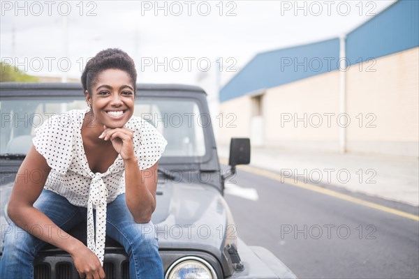 Smiling African American woman sitting on hood of car