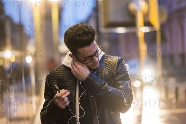 Caucasian man putting earbud in ear outdoors