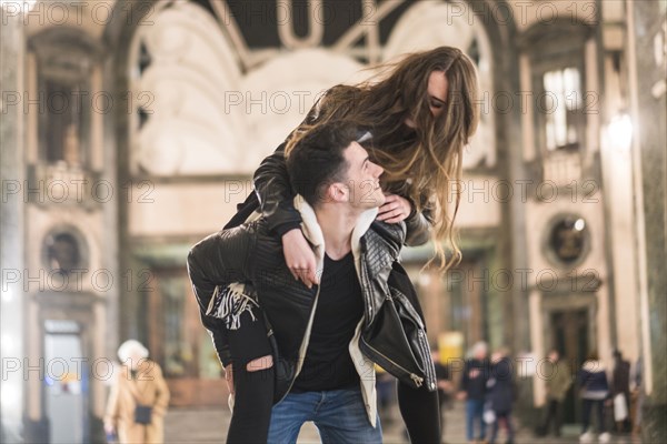 Caucasian man carrying woman piggyback in lobby