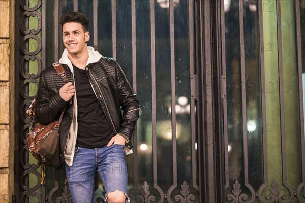 Smiling Caucasian man carrying bag leaning on gate