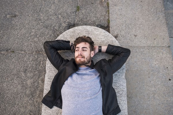 Caucasian man laying on concrete smoking cigarette