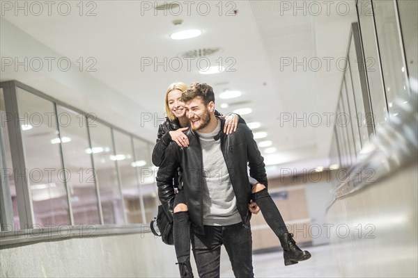 Caucasian man carrying woman piggyback in corridor