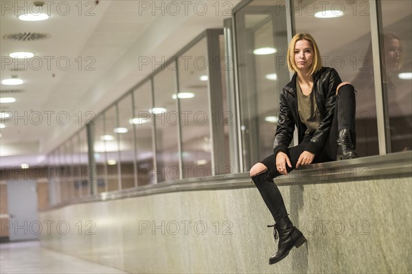 Caucasian woman sitting on ledge of window in corridor