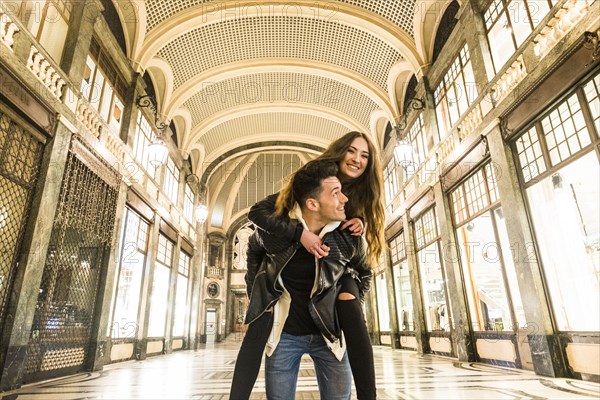 Caucasian man carrying woman piggyback in lobby