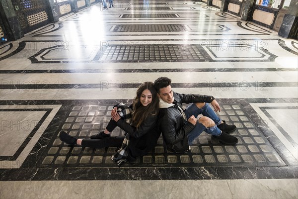 Caucasian couple sitting back to back on floor of lobby