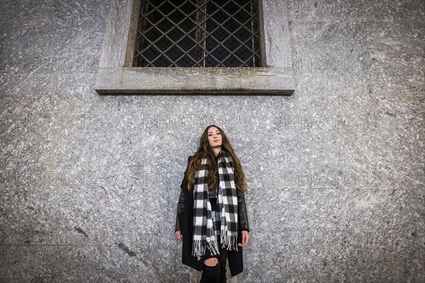 Serious Caucasian woman leaning on wall under window