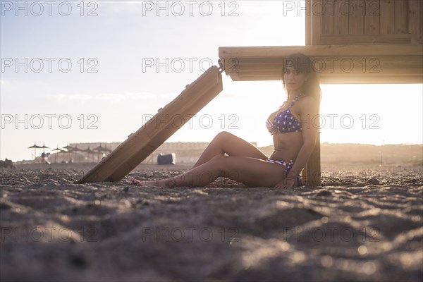 Caucasian woman sitting on beach leaning on cabana