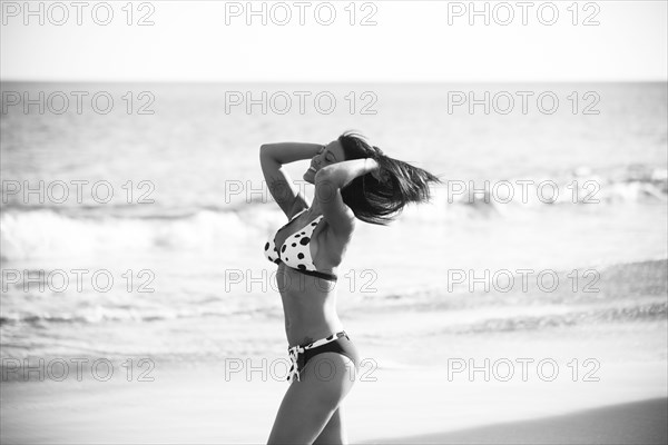 Caucasian woman walking on beach with hands in hair