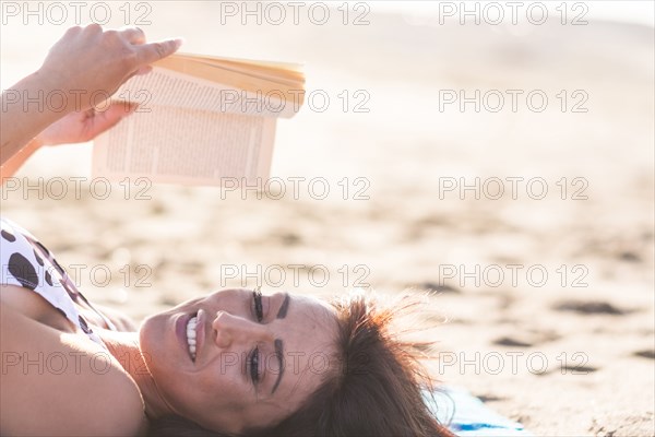 Caucasian woman laying on beach reading book