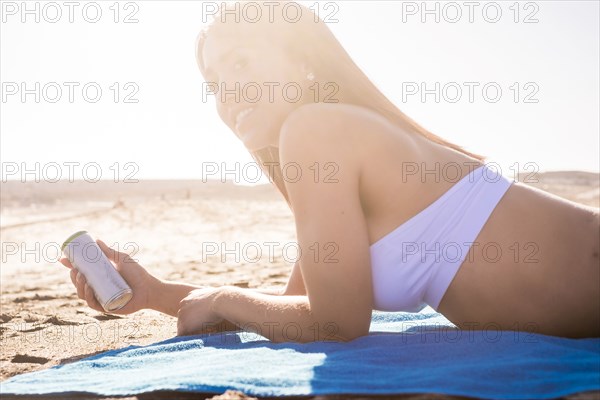 Caucasian woman laying on beach holding can