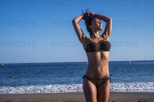 Caucasian woman standing on beach with hands in hair