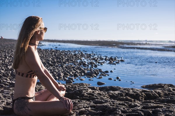 Caucasian woman sitting on beach wearing bikini