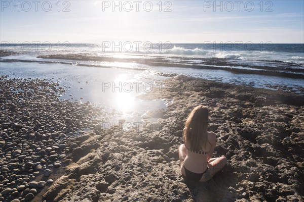 Caucasian woman sitting on beach wearing bikini