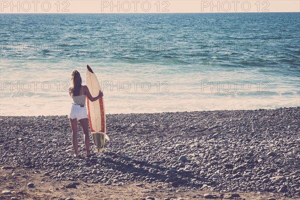 Caucasian woman standing on beach holding surfboard