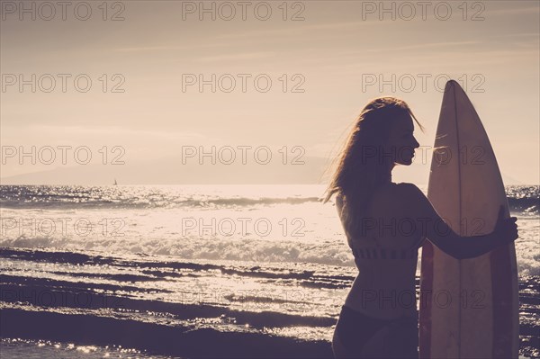 Caucasian woman standing on beach holding surfboard