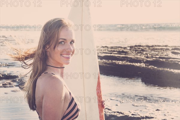 Caucasian woman standing on beach holding surfboard