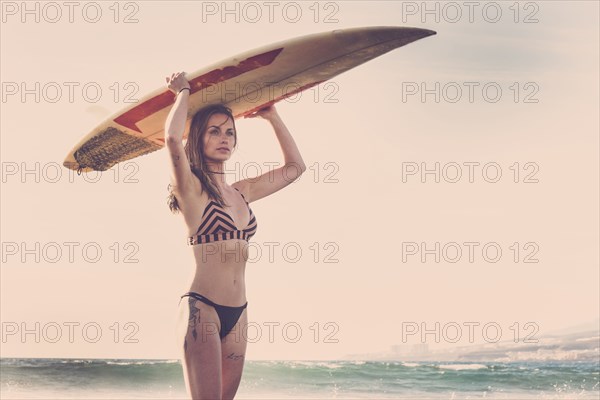 Caucasian woman standing on beach holding surfboard