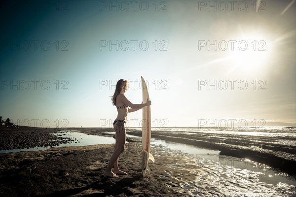 Caucasian woman standing on beach holding surfboard