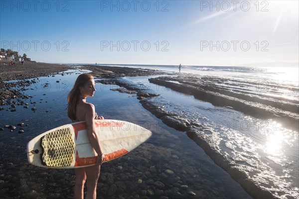 Caucasian woman standing on beach holding surfboard